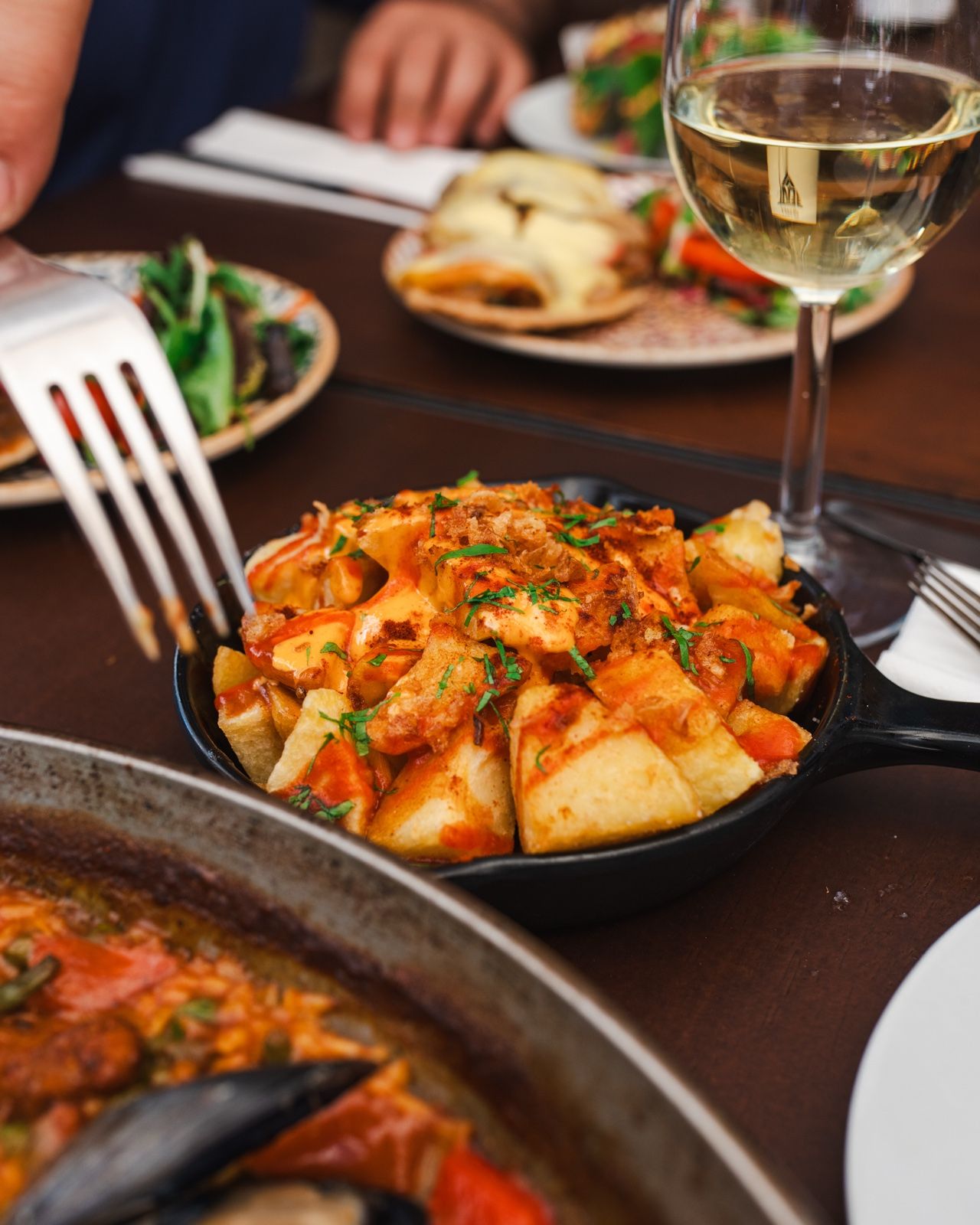 Patatas bravas mit Soße in der Pfanne, dazu ein Glas Weißwein