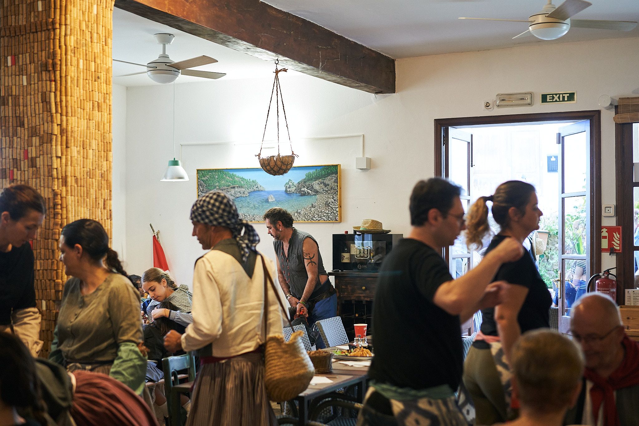 Interior del Bar Molino lleno de gente, con ventiladores de techo, lámpara de mimbre y un cuadro de una cala mallorquina.