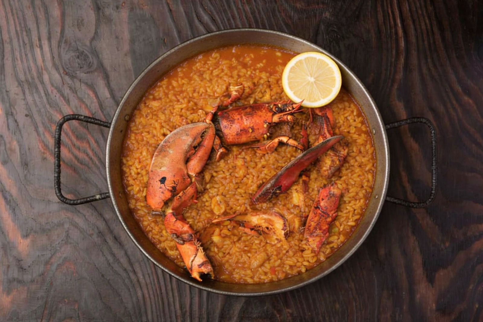 Arroz caldoso de bogavante recién hecho en una paellera de hierro, con piezas de bogavante y medio limón, visto desde arriba