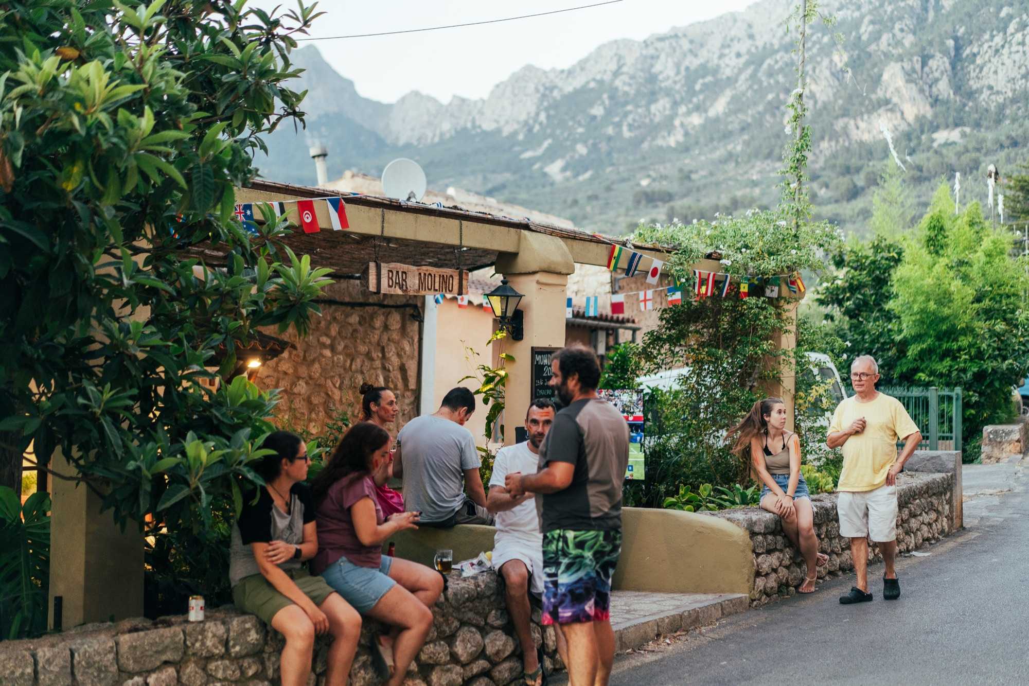 Terraza del Bar Molino llena de gente viendo el Mundial, con banderas y la Serra de Tramuntana al fondo